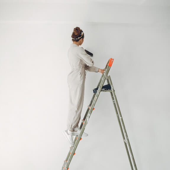 female on ladder painting large room white